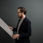 Man in black suit holding white paper