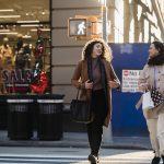 Cheerful young female shopaholics crossing road near fashion store in city