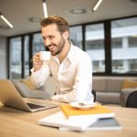 Depth of field photo of man sitting on chair while holding cup in front of table